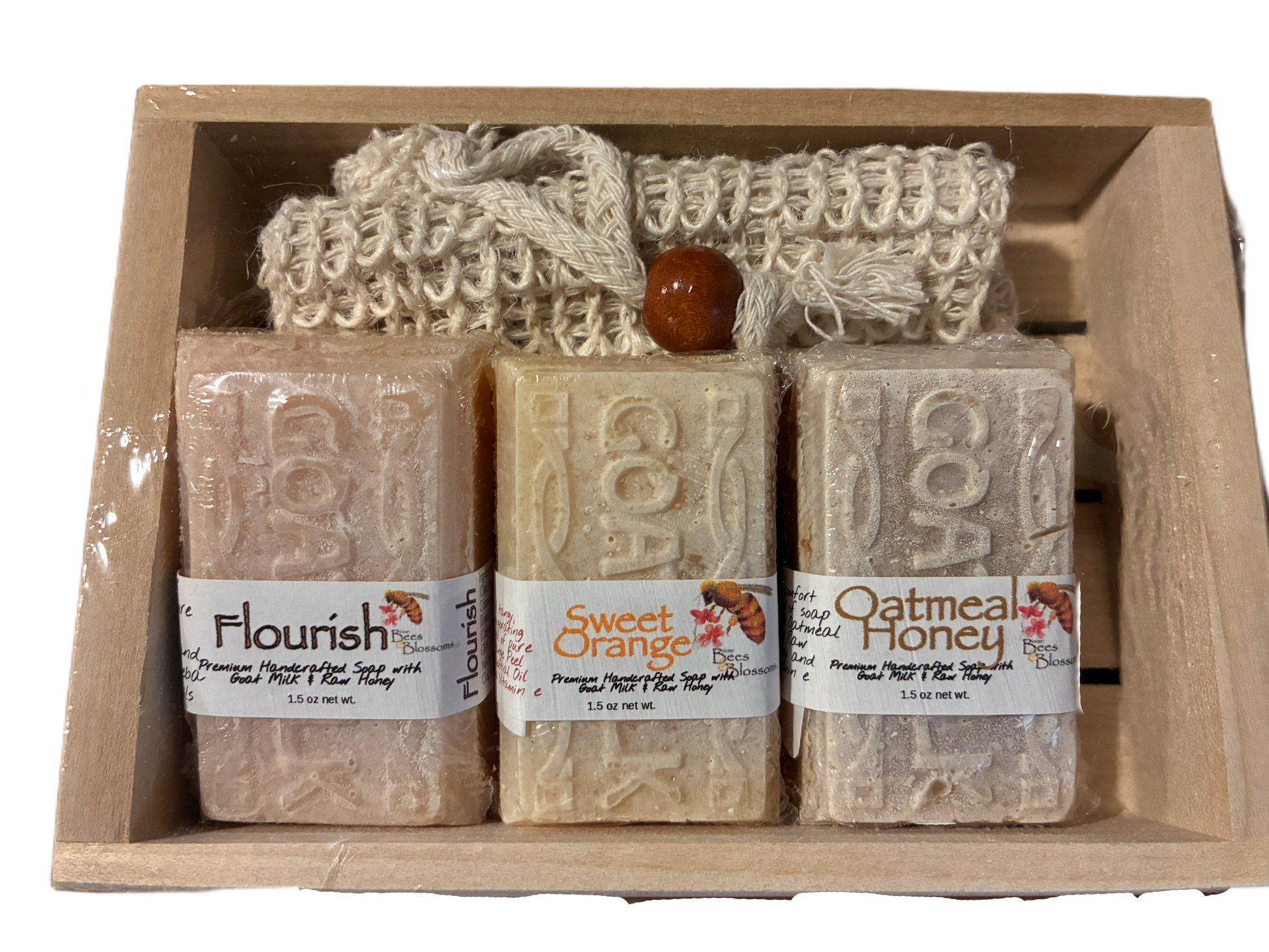 Three bars of soap with labels and a loofah in a wooden box.