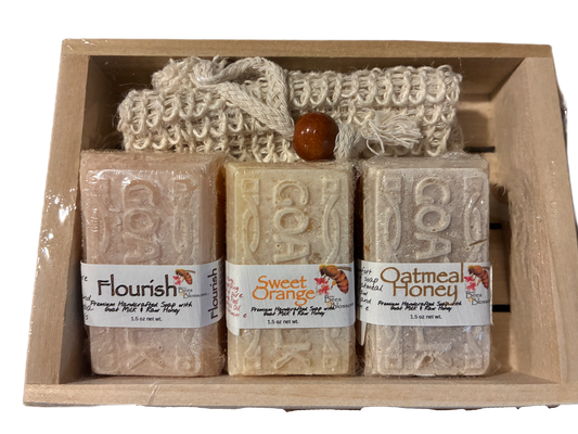 Three bars of soap with labels and a loofah in a wooden box.